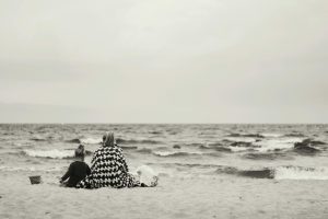 woman and child sitting on sand near body of water